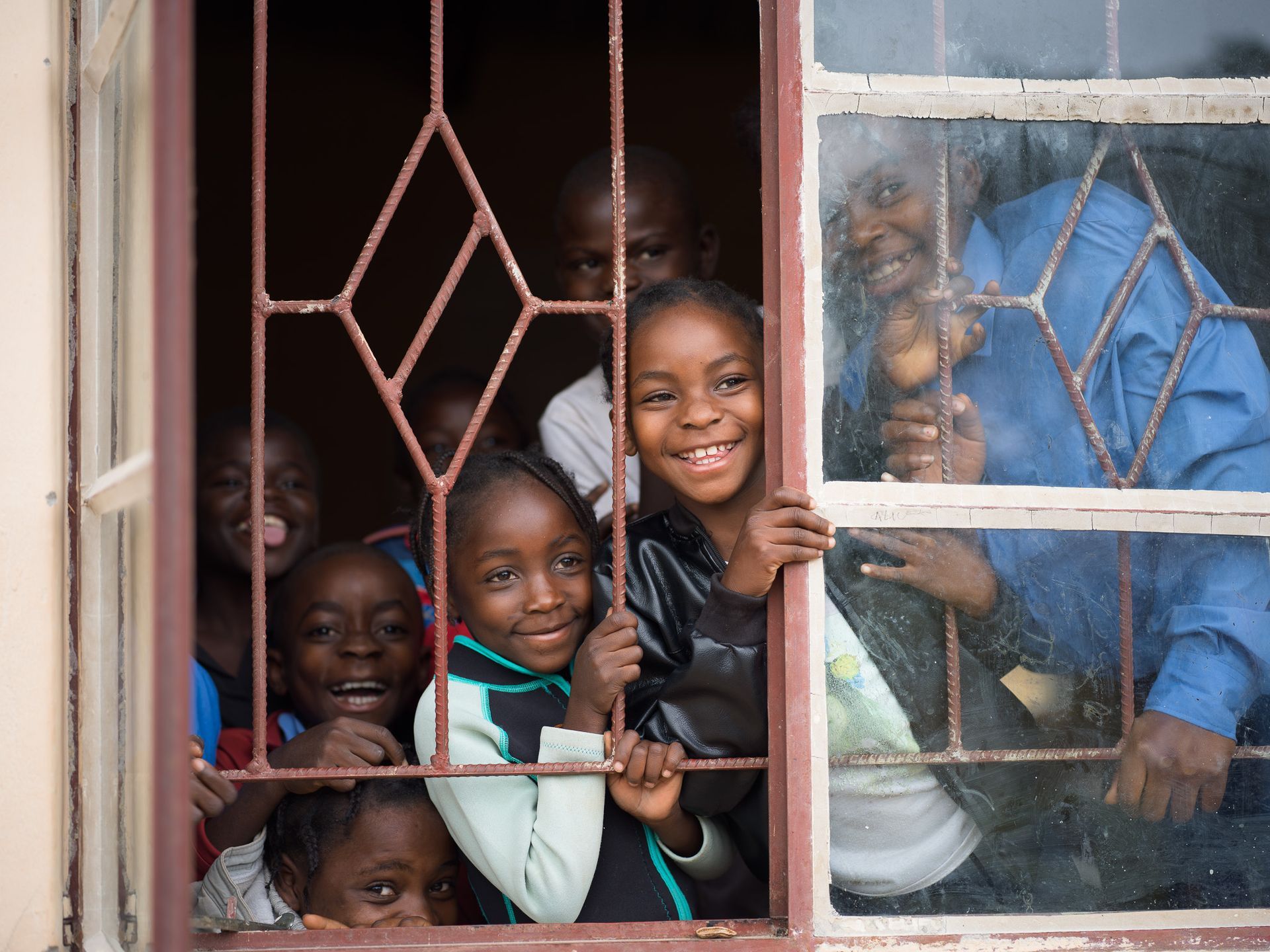 Children smiling through a window at Road 22 Community School, Meheba, Zambia